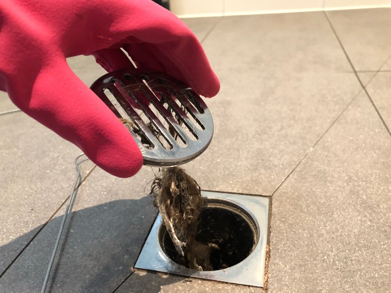 A person in red gloves is holding a drain strainer.